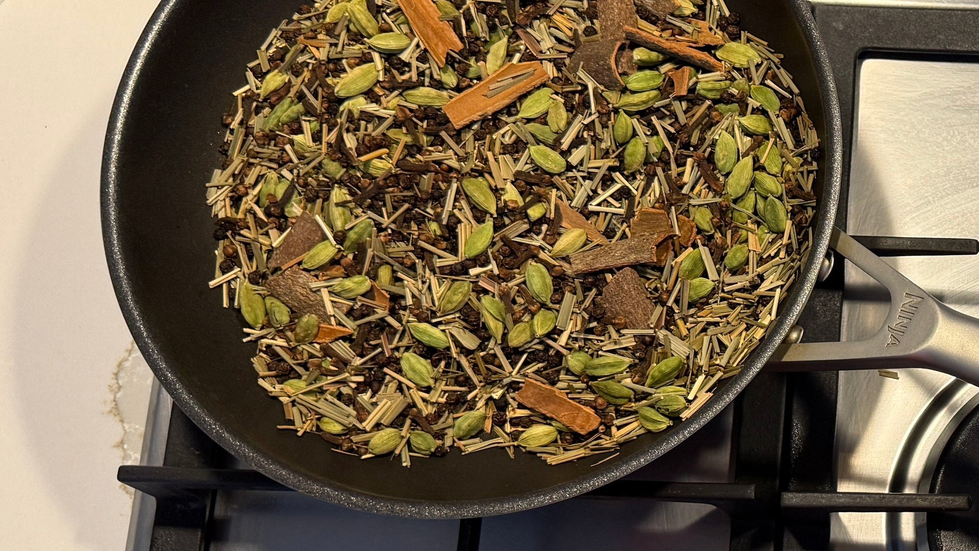 Frying pan on a gas stove with spices being cooked.